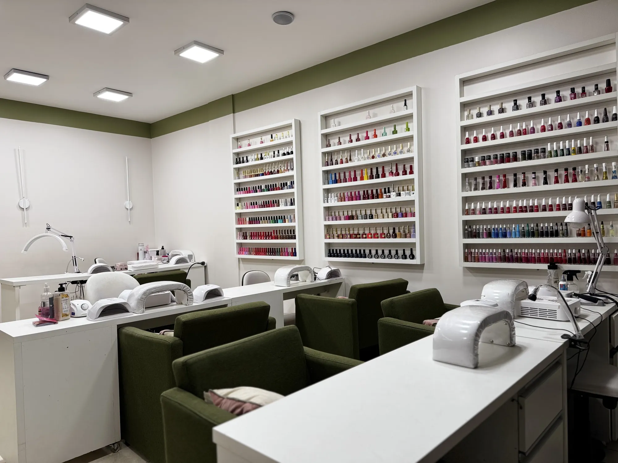 Estações de manicure com poltronas verdes e parede de esmaltes