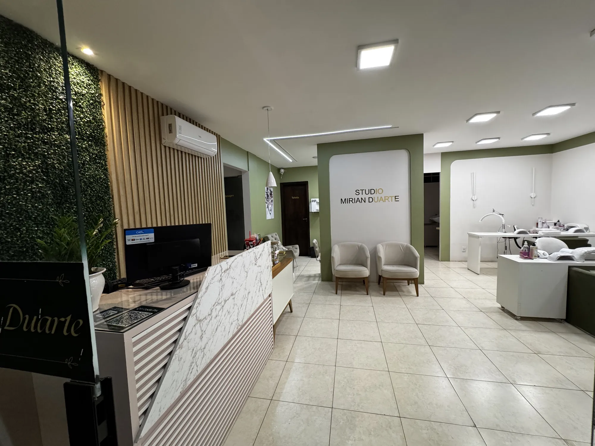 Recepção do Studio com poltronas claras, balcão e a logomarca na parede verde